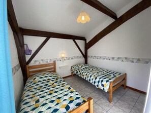 Une chambre à coucher avec deux lits en bois, une table de chevet, une lampe fixée au mur et un coussin à motifs géométriques.
