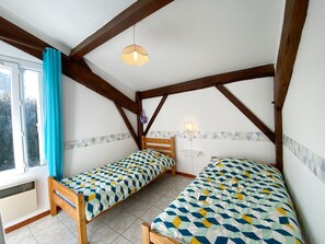 Une chambre avec deux lits simples, des poutres en bois, une fenêtre avec des rideaux et un luminaire suspendu.