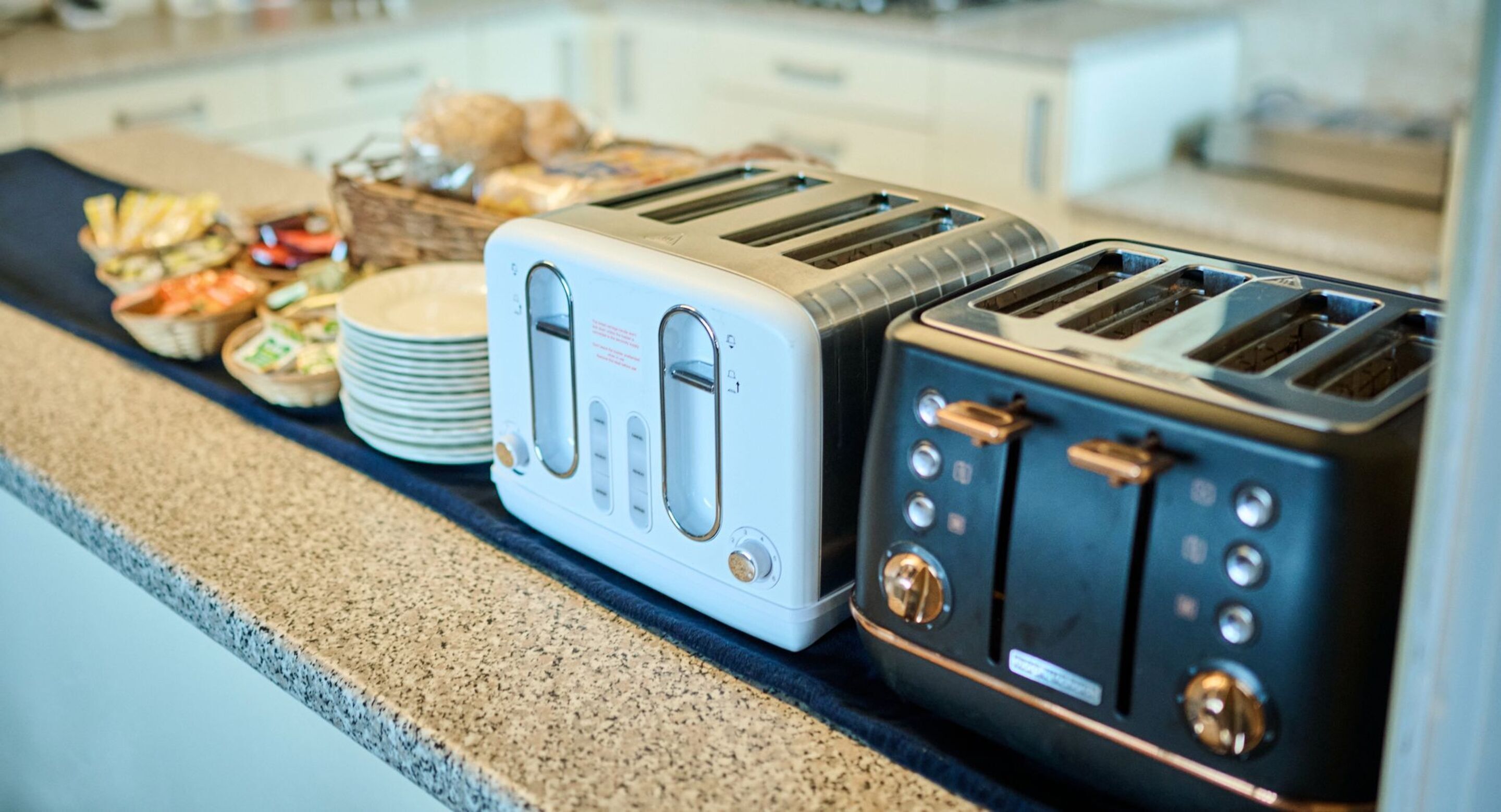 Two toasters on a kitchen counter with plates and food items.