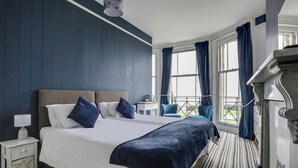 A hotel room with a large bed, a nightstand, a chair, and a view of the outdoors through large windows. - Lord Kitcheners Guest House (Lowestoft)