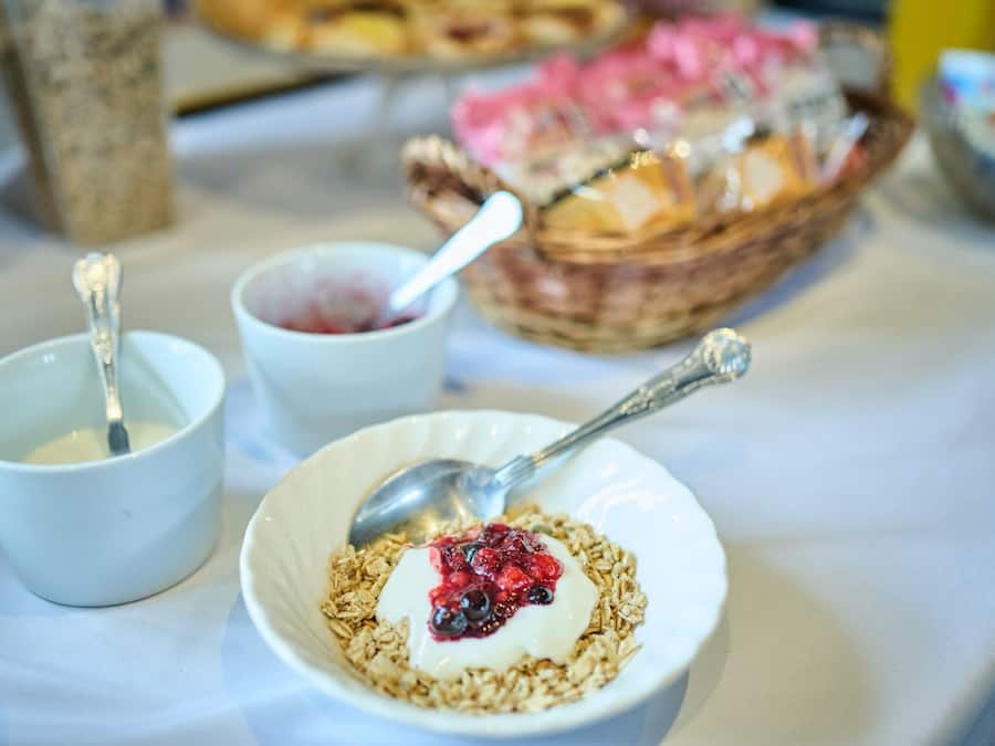 A breakfast setting with bowls of yogurt and granola, a spoon, and a basket of pastries.