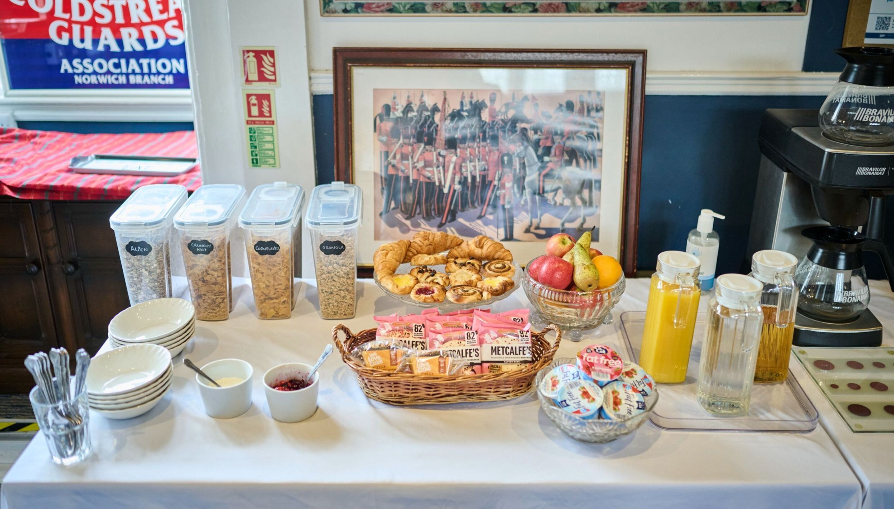 Un bufé de desayuno con diferentes alimentos, una máquina de café y un cuadro en la pared.