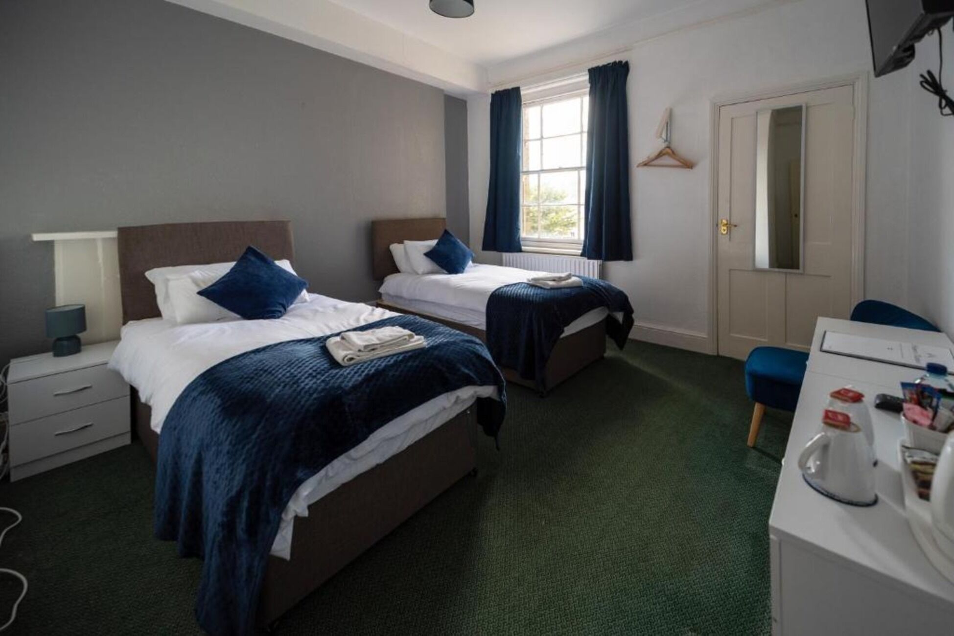 A hotel room with two beds, a desk, a chair, a mirror, and a window with curtains.