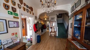 A hallway with wooden floors, a chandelier, coats on a rack, and a staircase. - Lord Kitcheners Guest House (Lowestoft)