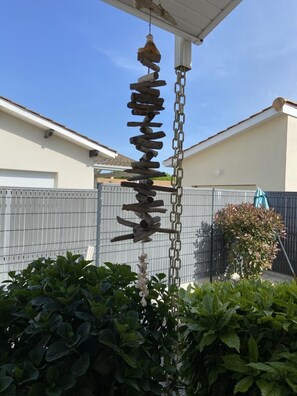 A vertical wooden structure with hanging elements, possibly a decorative piece, in a residential outdoor setting with a fence and greenery. - Gite DES Metairies - Hourtin (HOURTIN)