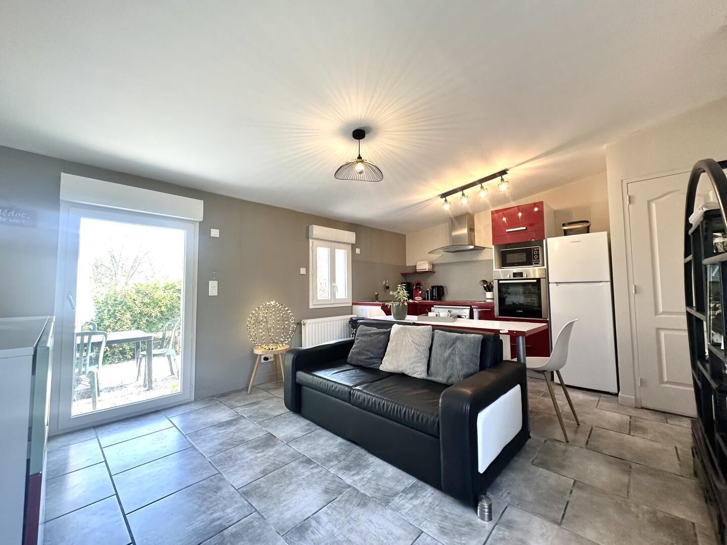 A modern kitchen with red cabinets, a black refrigerator, and a dining area with a table and chairs.