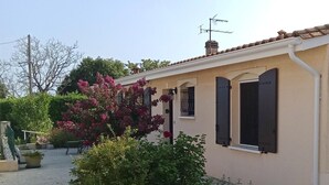 A building with a beige facade, a tiled roof, and a small garden with pink flowers. - Gîte Seguin - Eysines (EYSINES)