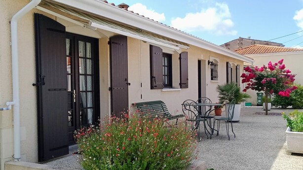 A building with a beige facade, dark shutters, and a gravel courtyard with a table and chairs. - Gîte Seguin - Eysines (EYSINES)
