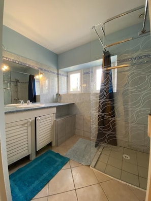 A bathroom with a glass shower enclosure, a sink with a mirror, and a blue towel on the floor.