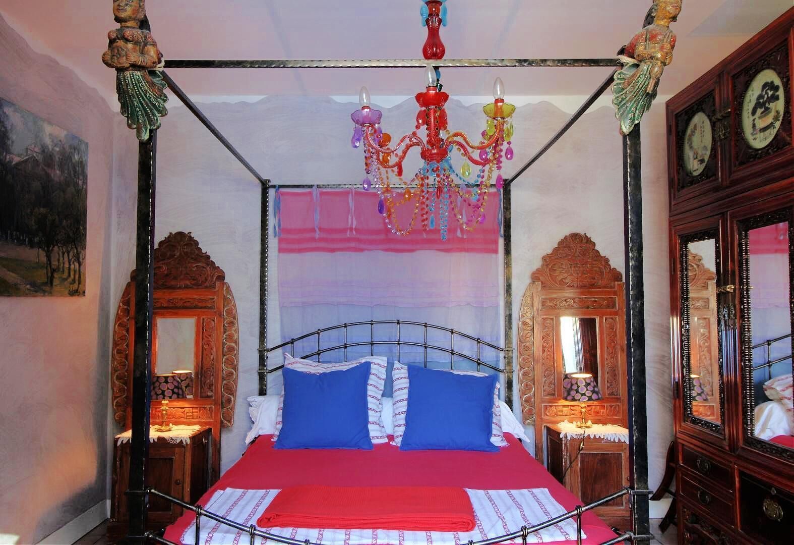 A four-poster bed with a red bedspread, blue pillows, and a hanging pink and purple tapestry.