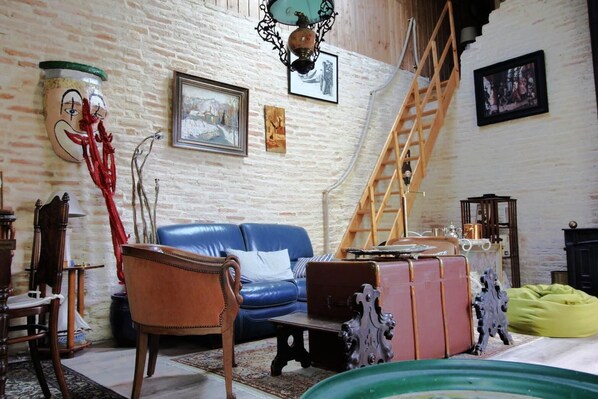 Une pièce avec un canapé bleu, une chaise en bois, une petite table, une échelle et un escalier.