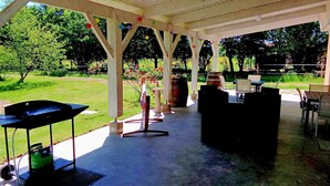 Une terrasse extérieure dotée d’un barbecue, d’un espace salon et d’une pergola illuminée de guirlandes lumineuses.