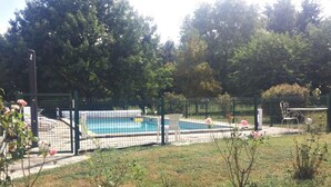 Un espace extérieur clos, doté d’une piscine, entouré d’arbres et d’une pelouse.