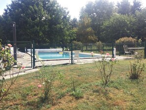 Un'area esterna recintata con piscina, circondata da alberi e un prato.