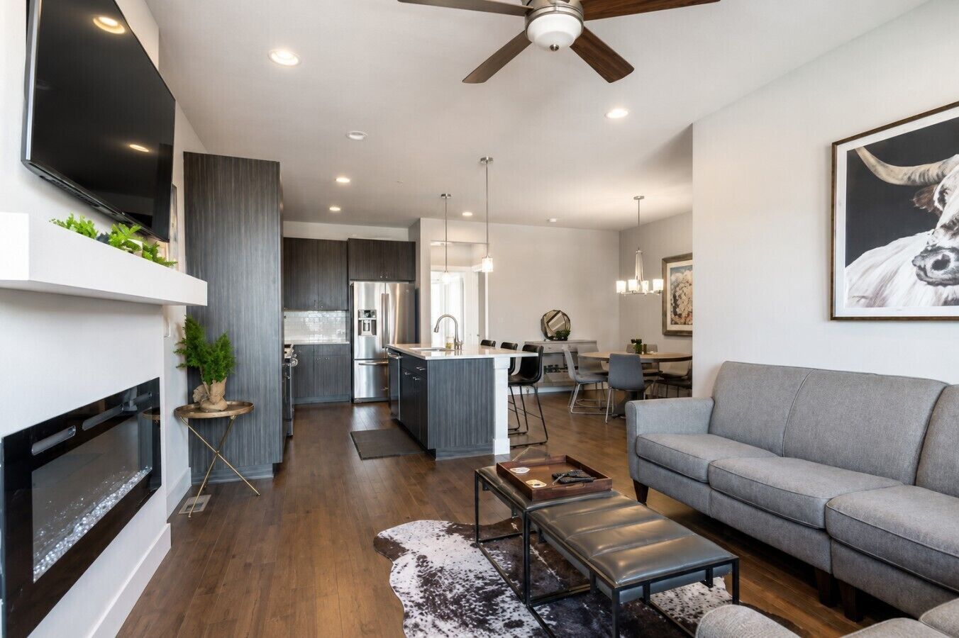 A modern living room with a fireplace, a grey sofa, and a dining area in the background.