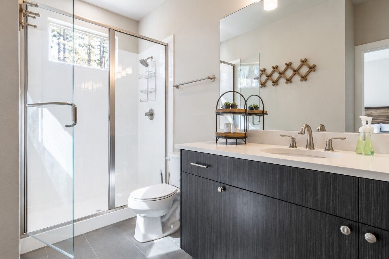 A modern bathroom with a glass shower enclosure, a toilet, a vanity with dark wood cabinets, and a mirror with a wooden wall-mounted rack.