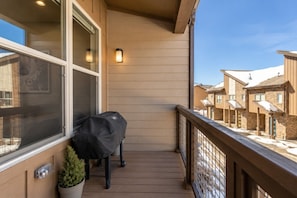 A balcony with a grill, potted plant, and a view of neighboring buildings.