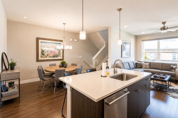 A modern kitchen with a central island, dining area with chairs, and a staircase leading to another level.