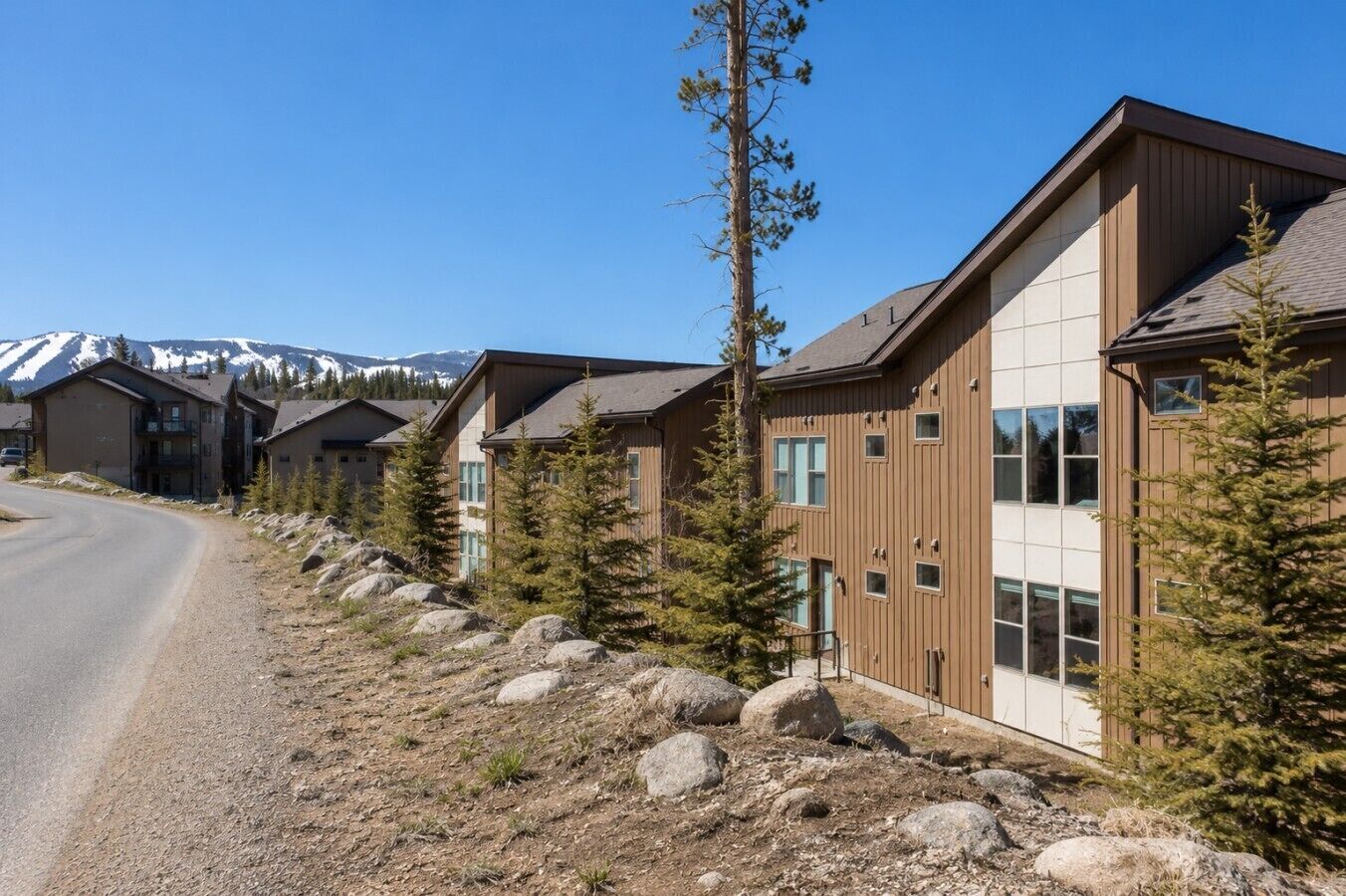 A row of modern buildings with large windows, a clear sky, and a mountain range in the background.