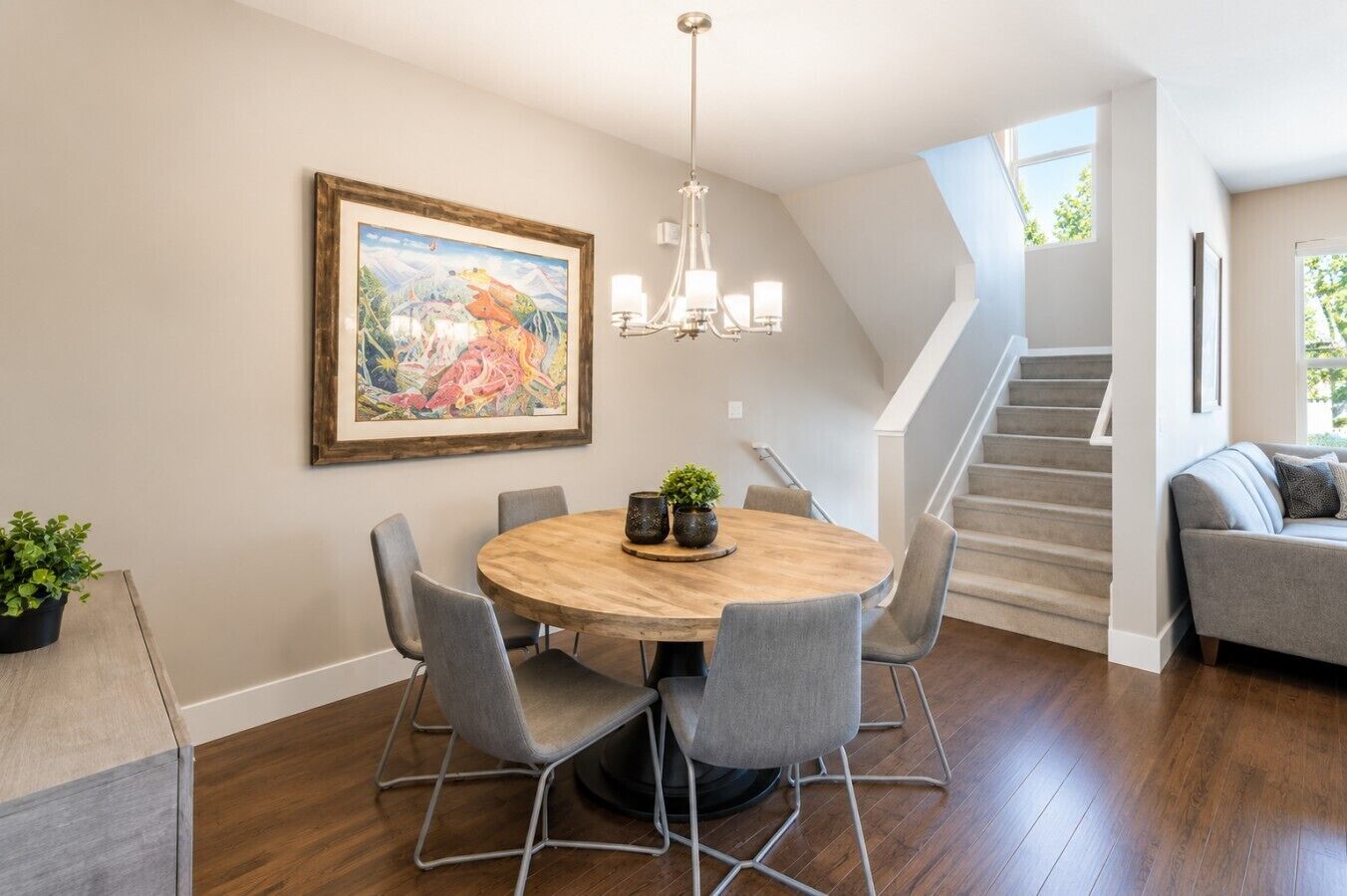 A dining area with a round table, chairs, a chandelier, and a staircase leading to another level.