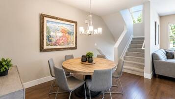 A dining area with a round table, chairs, a chandelier, and a staircase leading to another level.