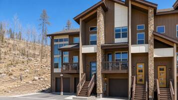A multi-story building with a stone facade, balconies, and a parking area.