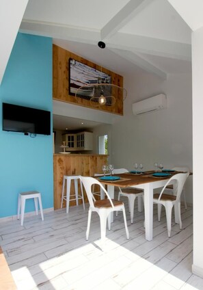 A dining area with a wooden table and white chairs, a kitchen area with wooden cabinets, and a mounted television.