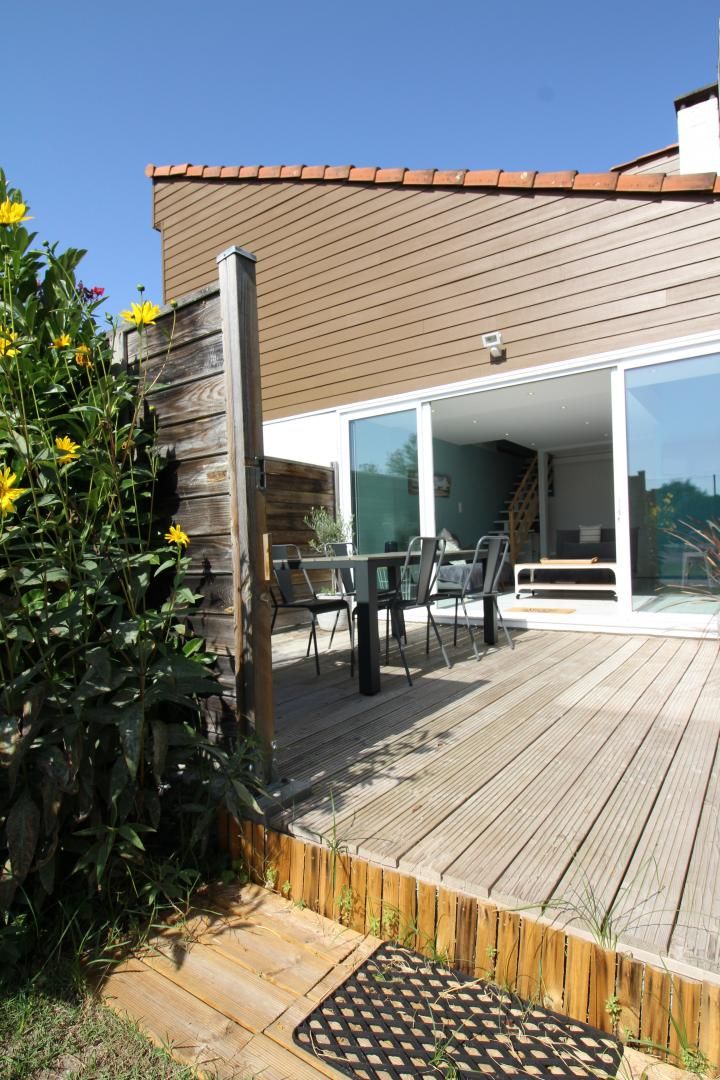 A wooden deck with a table and chairs, a sliding glass door leading to an interior space, and a wooden fence with plants.