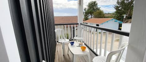 A balcony with white plastic chairs and a small table, overlooking a residential area with houses and trees.