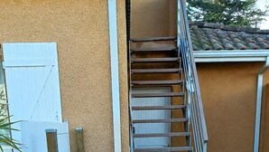 Eine Treppe führt zu einem Gebäude mit hellbeige Fassade, einer weißen Tür und einem Metallgeländer.