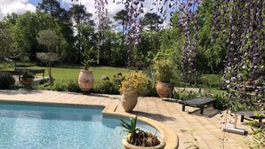 A pool with a surrounding patio area, large planters, and a view of the surrounding greenery.
