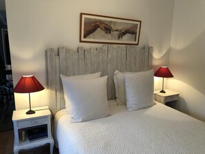 Ein Bett mit weißer Bettwäsche, zwei Nachttische mit Lampen, ein Holz-Kopfteil und ein gerahmtes Kunstwerk darüber.
