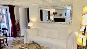 A cozy living room with a white sofa, a wicker basket with a number, a patterned rug, and a large mirror on the wall.