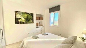 Een slaapkamer met een bed, nachtkastje, raam en een plank met decoratieve spullen.