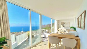 Een moderne woonkamer met een grote schuifglazen deur die leidt naar een balkon met uitzicht op zee.