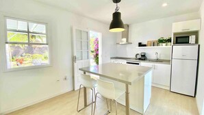 Een moderne keuken met een centraal eiland, witte kasten en een raam met uitzicht op groen.