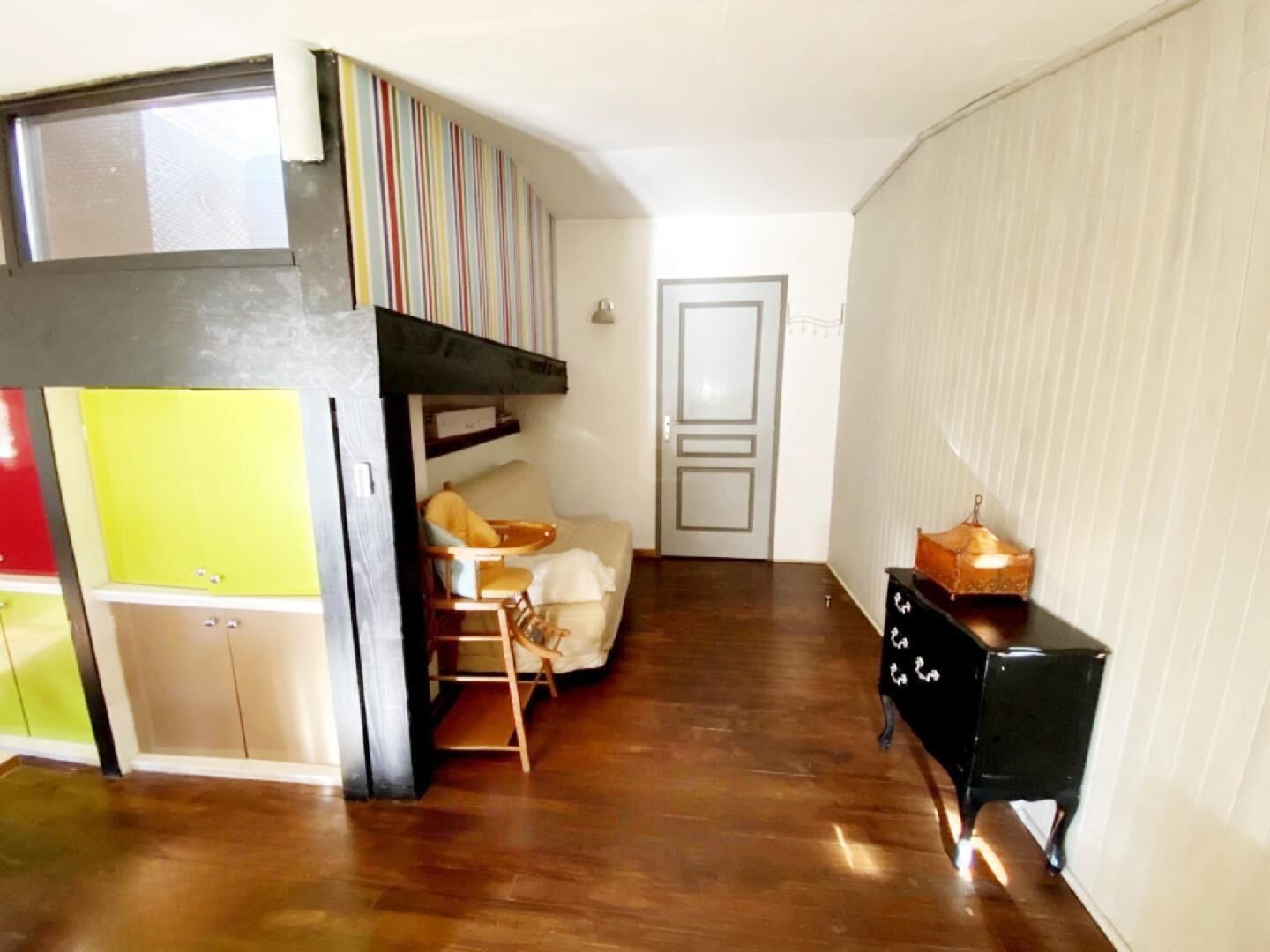 Ein kompakter Wohnraum mit Etagenbett, einer Küchenzeile, einer kleinen Essecke und einer Tür zu einem weiteren Raum.