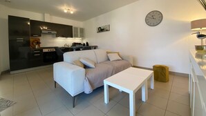 Eine moderne Wohnung mit Küche, einem Wohnbereich inklusive Sofa und Couchtisch, einer Uhr an der Wand und einer Lampe auf dem Nachttisch.