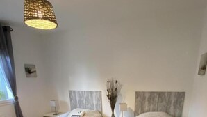 Ein Hotelzimmer mit zwei Betten, einem Nachttisch mit Lampe, einer Vase mit getrockneten Blumen und einer Pendelleuchte.