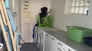 Ein Waschraum mit Waschmaschine, Wäscheständer und gestapelten Holzbrettern.