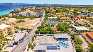 An aerial view of a coastal town with a prominent hotel featuring a swimming pool, a beach, and a road running through the area.