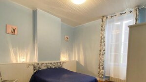 A room with a bed, a chair, a radiator, and a window with curtains. - Gite DU Jardinet - Saint-andre-du-bois (SAINT-ANDRE-DU-BOIS)