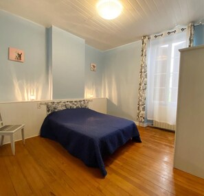 Um quarto com cama, cadeira, radiador e janela com cortinas.