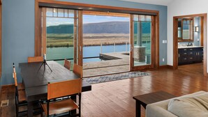 Amplia habitación con un gran ventanal corredero que da a un balcón con vistas a un lago y montañas.