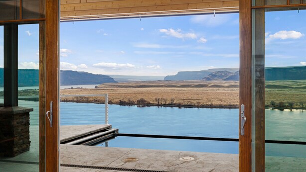 Vista desde una habitación con puerta de cristal que da a una piscina, con vistas a un paisaje de montañas y una masa de agua.