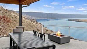 Un patio al aire libre con una mesa y sillas, un pozo de fuego y vistas a un lago y montañas.