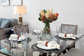 Mesa de jantar posta com copos transparentes, pratos e guardanapos, com um vaso de flores no centro.