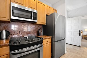 A kitchen with wooden cabinets, a stainless steel microwave, a refrigerator, and a stove. - Grand Champions | Ocean View 2 BR | Car Incl. w/ 6+ Nights | GCH-120 by KBM (Wailea)