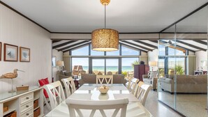 A spacious dining area with a large table, white chairs, and a view of the beach through large windows. - Gulf Front 3bd/2ba Home With Private Beach Access! (Panama City Beach)