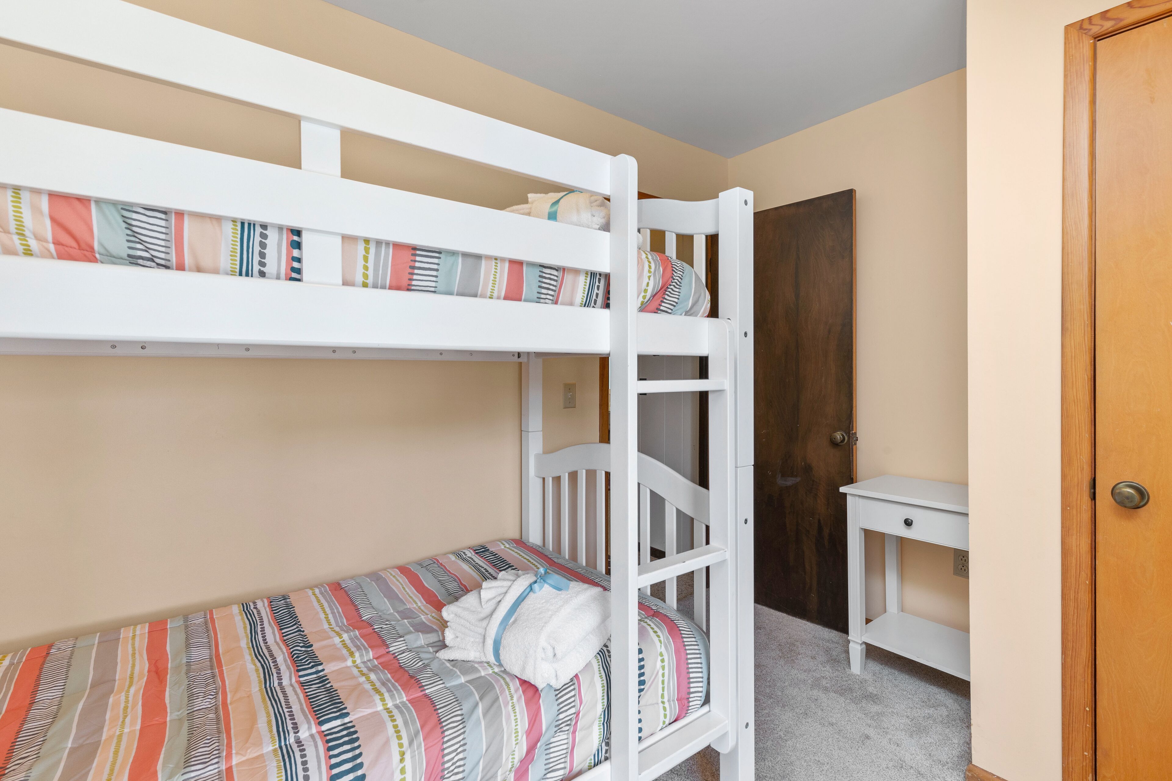 A bunk bed with a striped bedspread and a white bedside table.